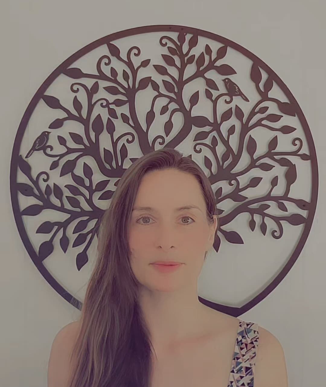 Woman with long brown hair centered before a large circular metal tree wall sculpture.